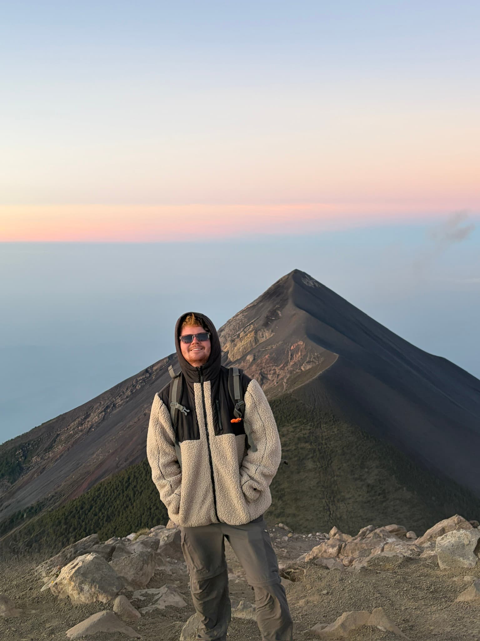 Toby Johnston standing on a summit at sunset, volcanic peak behind him