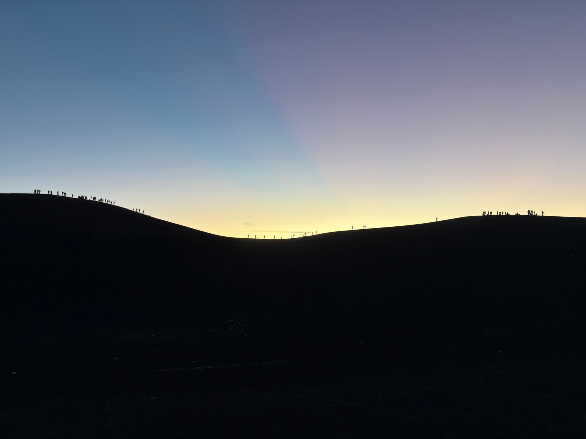 A line of hikers silhouetted along a ridge at dusk