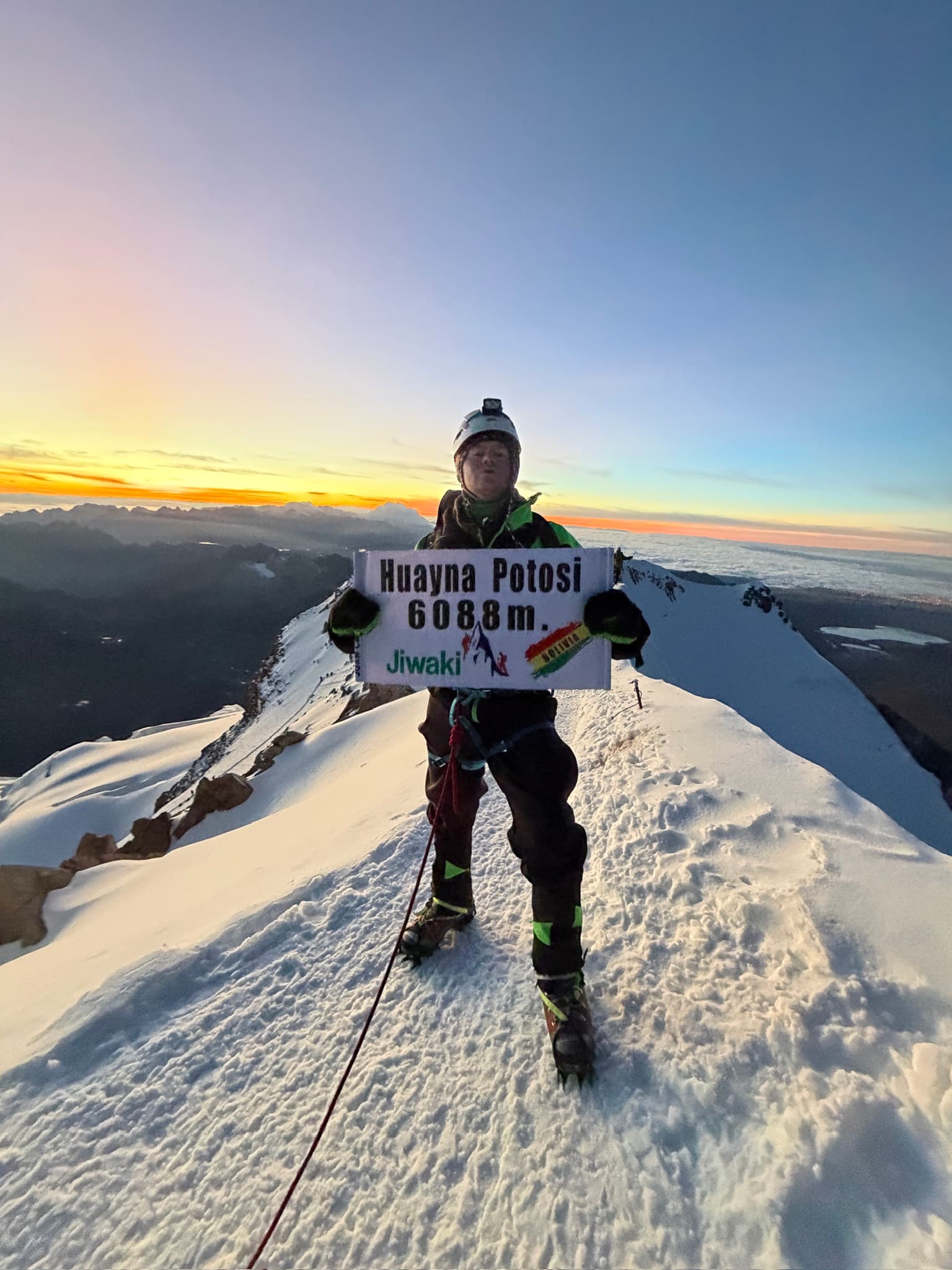 Standing on the summit ridge of Huayna Potosi at sunrise holding a summit sign