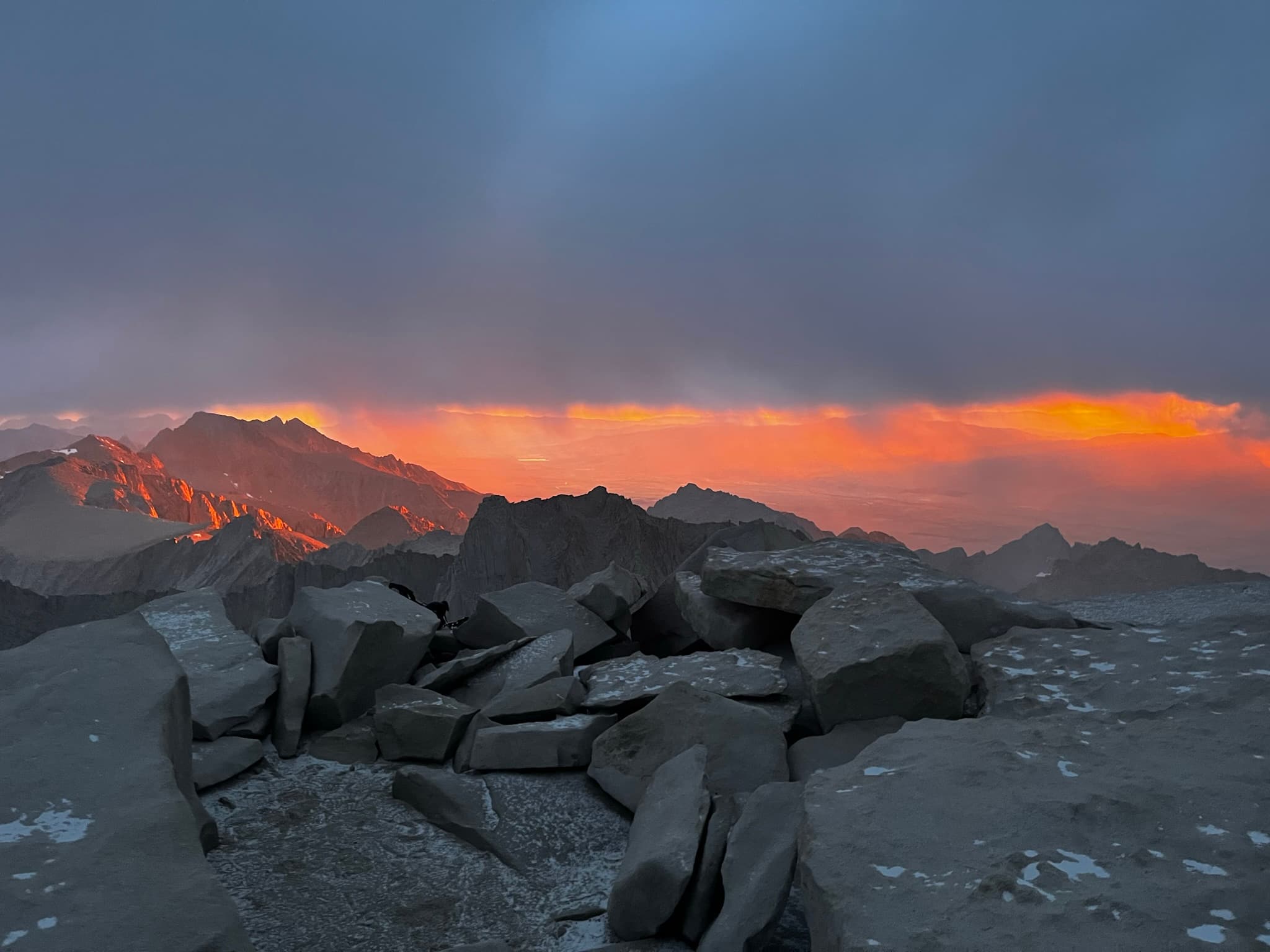 Storm clouds glowing orange at sunset over a rocky mountain ridge